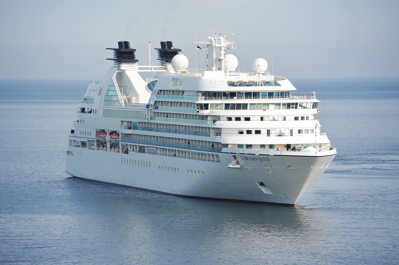 Large white cruise ship with dark funnels sailing on calm blue sea under a pale sky